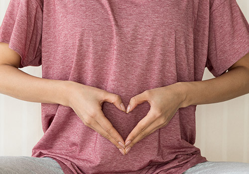 person holding hands in shape of heart over stomach